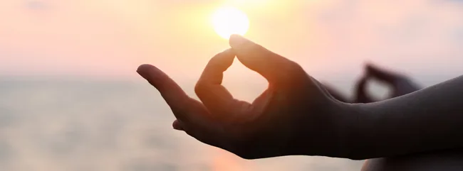 Hand in Meditationshaltung vor dem Sonnenuntergang