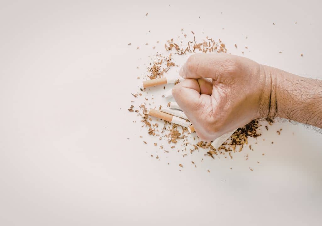 Hand zerdrückt Zigaretten als Symbol für Willenskraft und den Versuch, mit dem Rauchen aufzuhören
