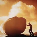 Mann versucht einen großen Stein zu schieben als Symbol für Motivation beim Rauchstopp