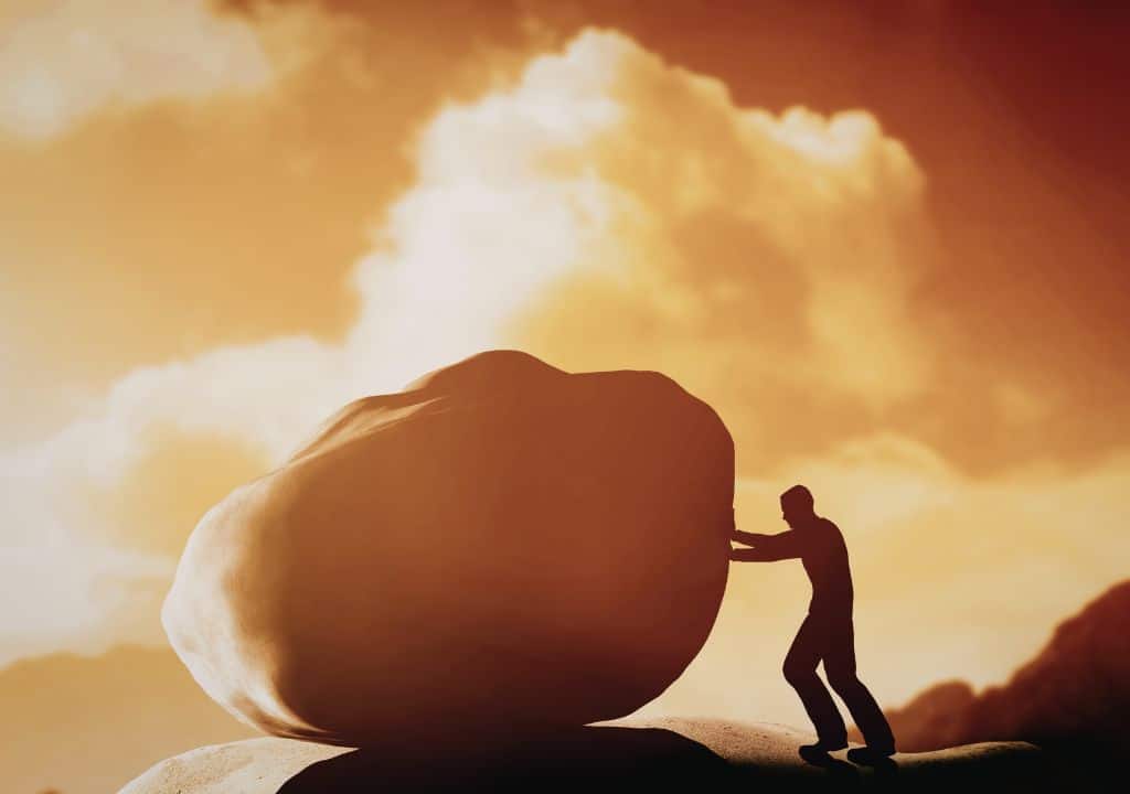 Mann versucht einen großen Stein zu schieben als Symbol für Motivation beim Rauchstopp