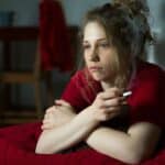 Frau sitzt nachdenklich auf dem Sofa und hält eine Zigarette in der Hand – typischer Moment eines Rückfalls beim Rauchstopp durch innere Gedanken und Trigger