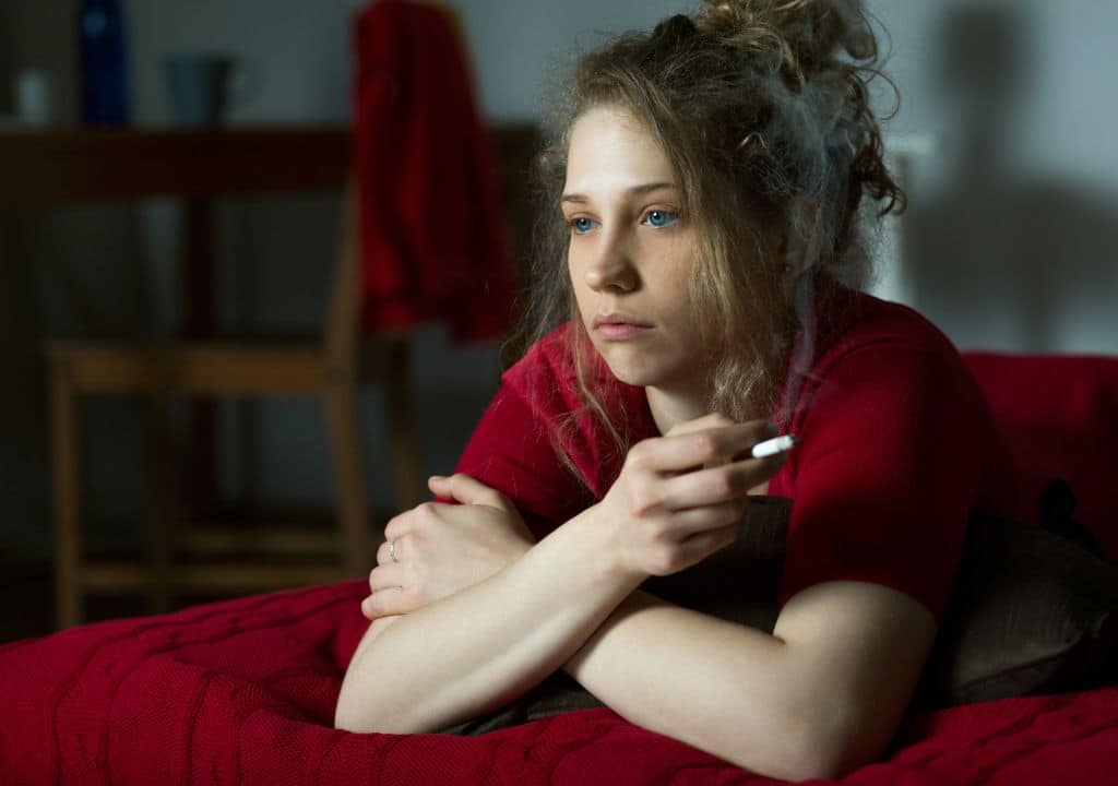 Frau sitzt nachdenklich auf dem Sofa und hält eine Zigarette in der Hand – typischer Moment eines Rückfalls beim Rauchstopp durch innere Gedanken und Trigger