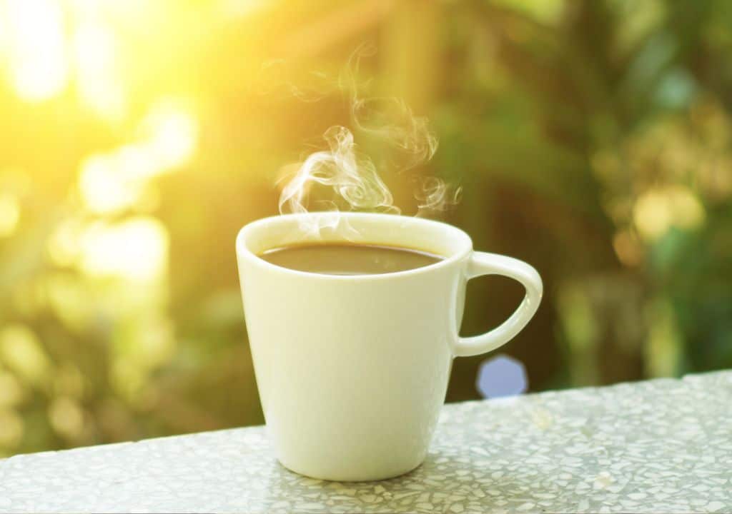 Dampfende Tasse Kaffee auf einem Tisch im warmen Morgenlicht als Symbol für ein neues Morgenritual ohne Zigarette.