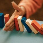 Hand stoppt eine Reihe fallender Dominosteine